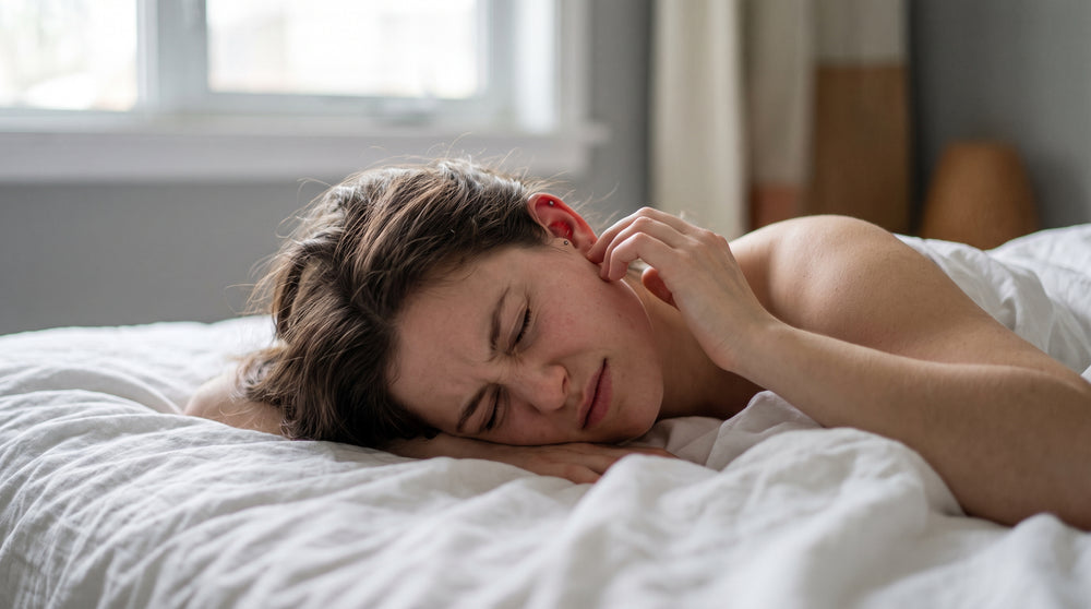 Junge Frau hebt morgens den Kopf vom Bett und berührt vorsichtig ihr Ohr
